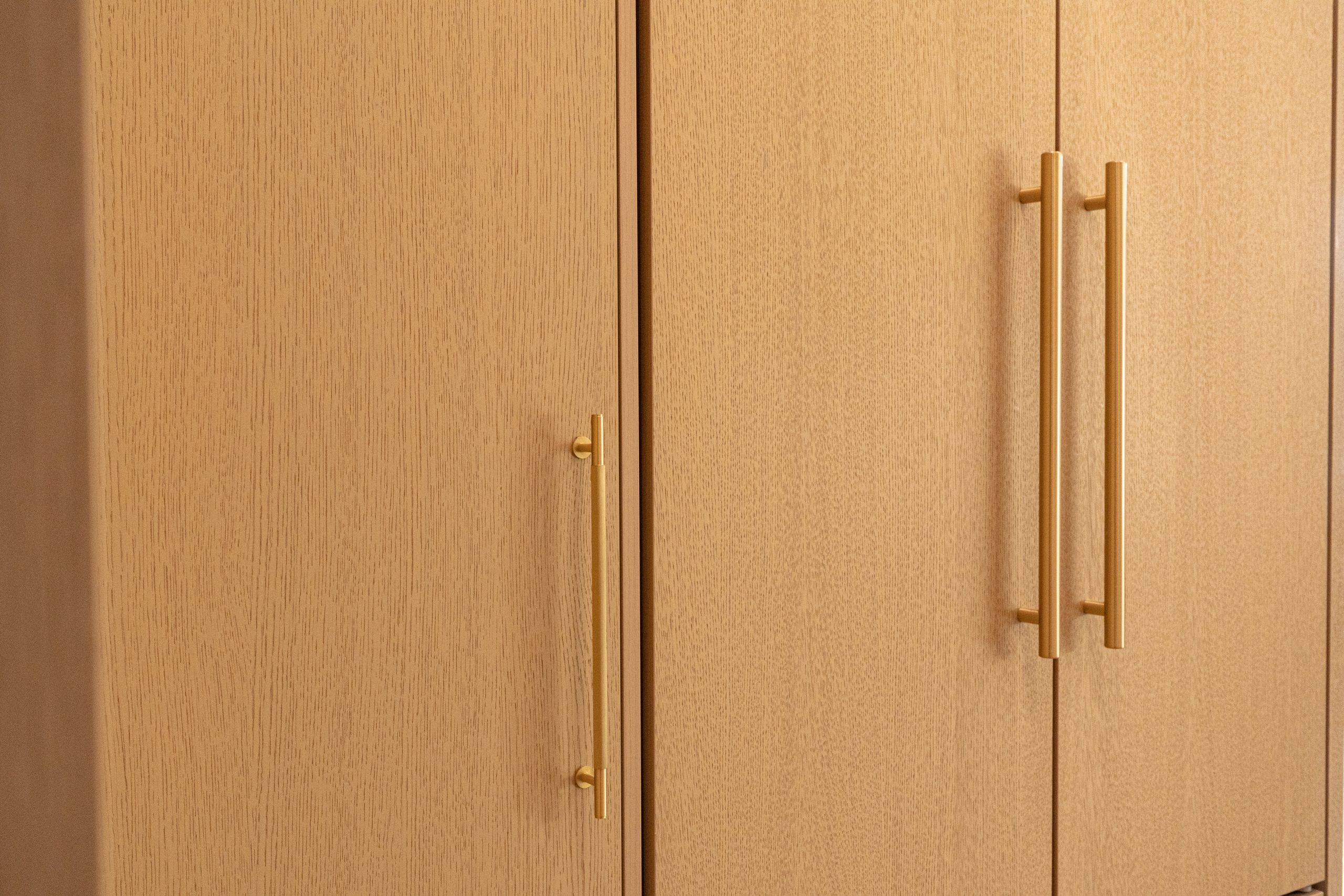 Custom cabinet doors with brushed gold bar handles and natural wood veneer finish by Forma Fine Cabinetry